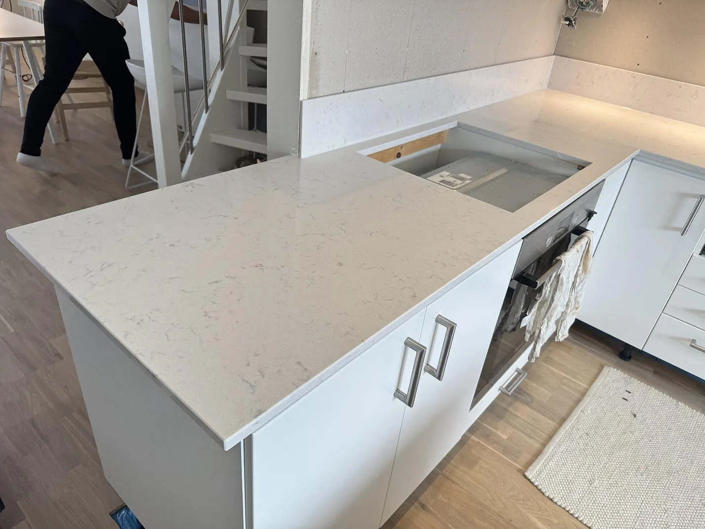 Polerad köksbänkskiva i Silestone Lagoon med hällöppning, låg väggsten och vita skåp i ett kök i Växjö.
