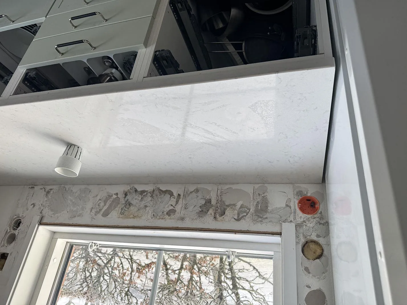 Detalj av polerad Silestone Lagoon i kök, med reflekterande ljus yta och väggytor under arbete vid fönster i Varberg.