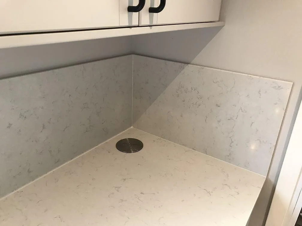 Köksbänkskiva i krämvit Silestone Lagoon, polerad, med heltäckande stänkväggar i hörn och infällt runt eluttag i ett kök i Veberöd.