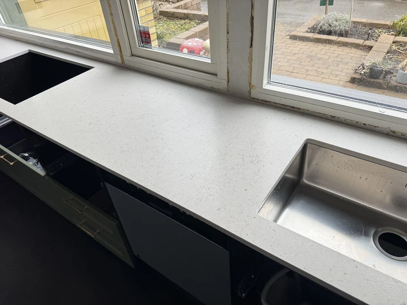 Köksbänkskiva i krämvit Silestone Lime Delight, matt Mocka-finish, längs fönster i ett kök i Åkarp med underlimmad rostfri diskho och salviegröna luckor.