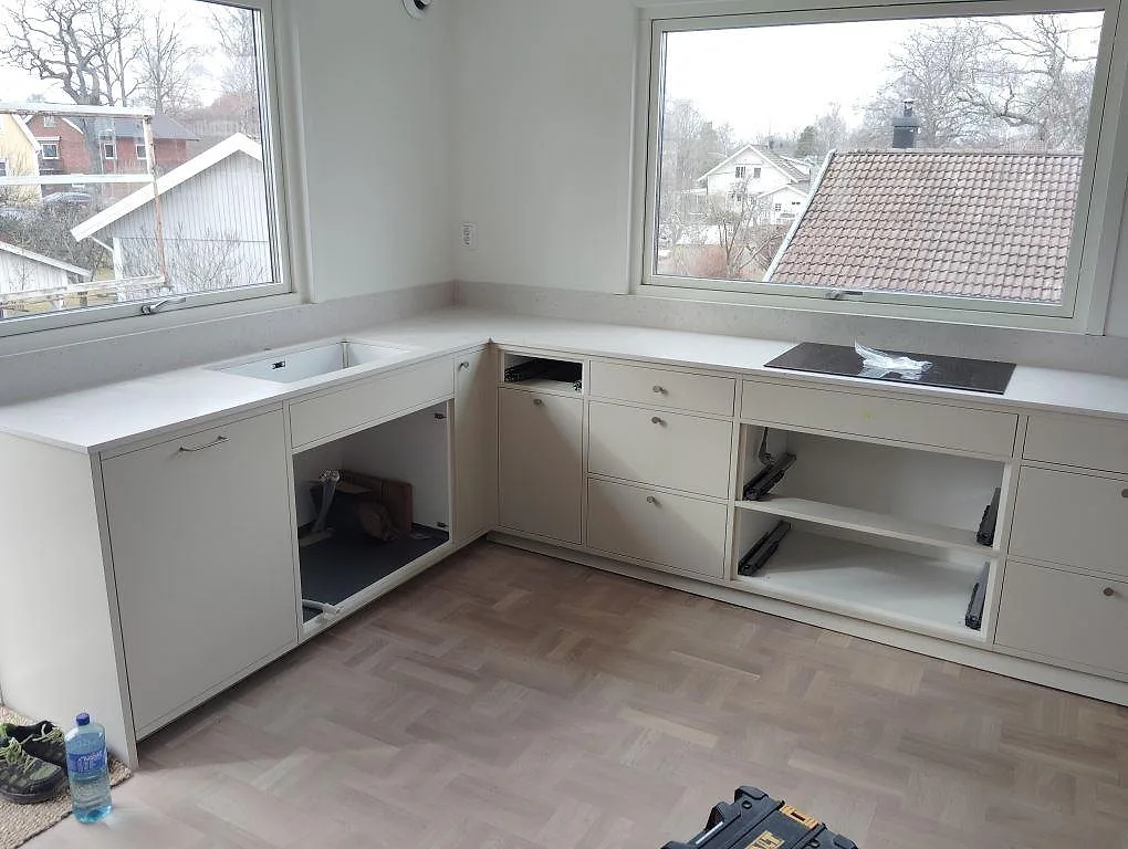 Köksbänkskiva i matt Silestone Lime Delight, komposit, med låg stänkkant i ett U-format kök med stora fönster i Älvsjö.
