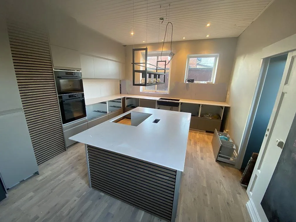 Översiktsbild av kök i Anderslöv med stor köksö och väggbänkar i matt Silestone Lime Delight komposit.
