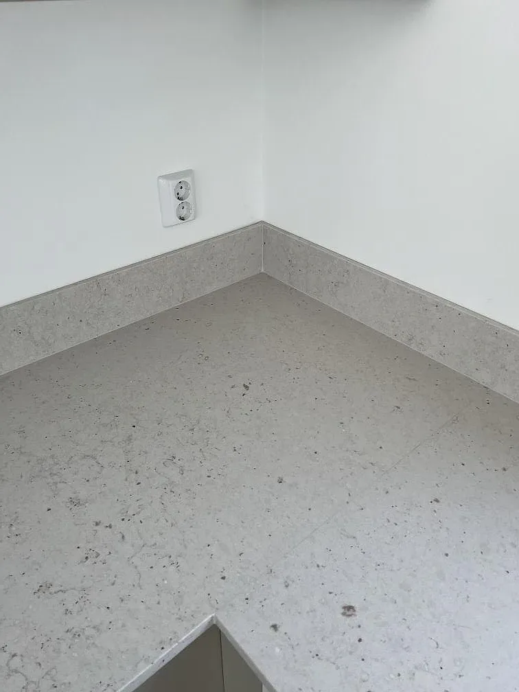 Hörn av köksbänkskiva i matt Silestone Lime Delight med låg stänkkant och eluttag i Borgholm.