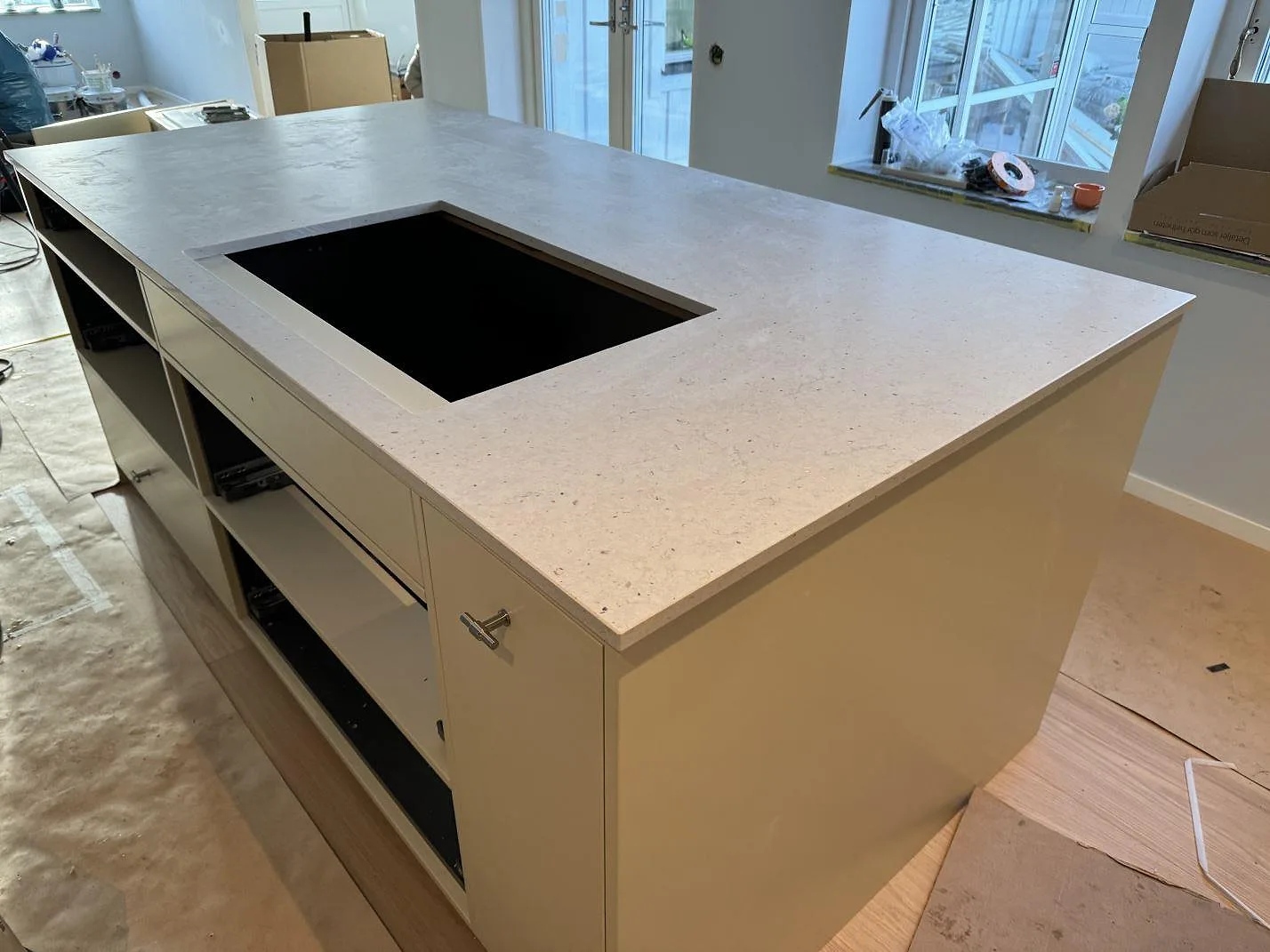 Köksö i ljus Silestone Lime Delight, matt komposit, med öppning för häll och vita köksstommar i Höganäs.