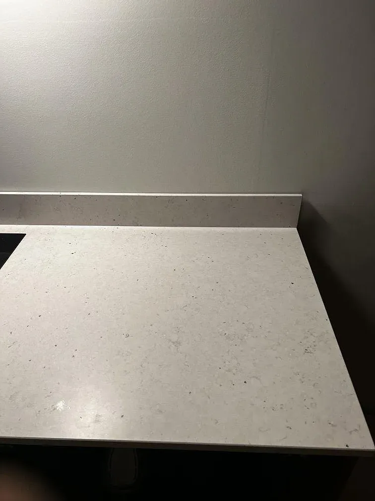 Ljus bänkskiva i Silestone Lime Delight med låg stänkkant och matt stenbild under väggbelysning i ett kök i Malmö.