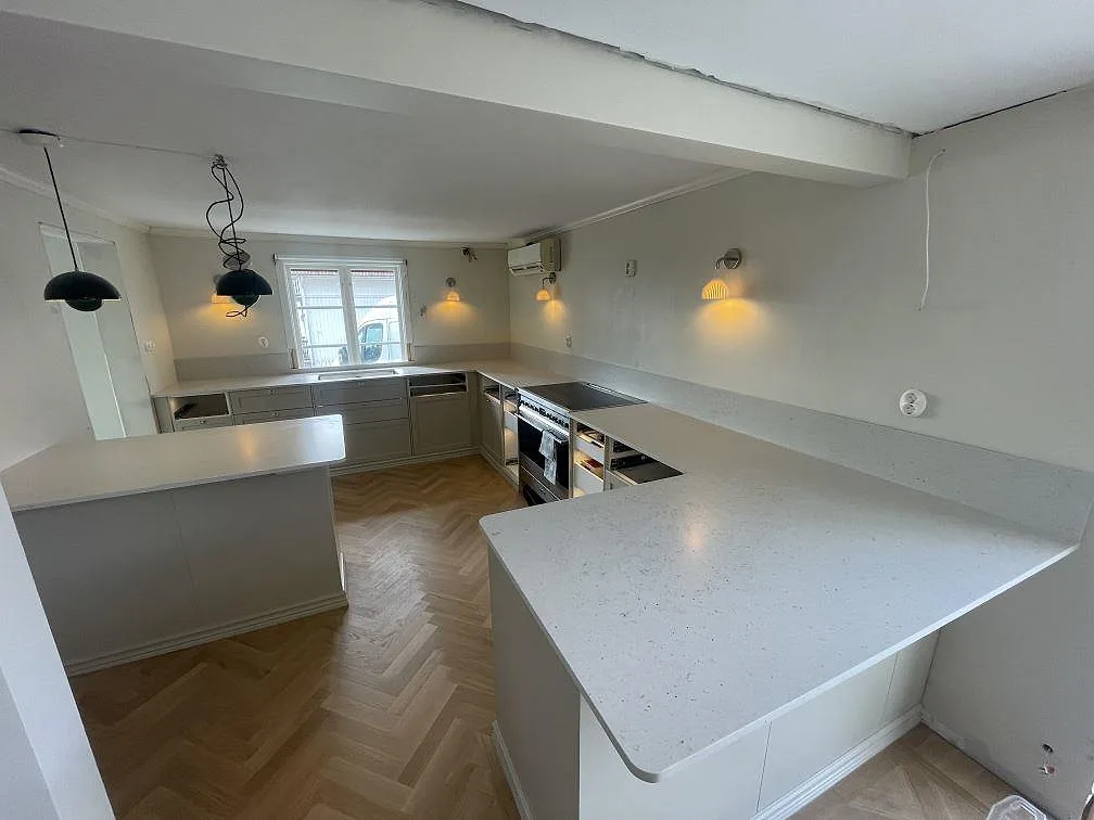 Köksbänkskiva i gräddvit Silestone Lime Delight, matt Mocka, i ett U-format kök med halvö och herringbone-parkett i Mullsjö, fotograferat under montering.