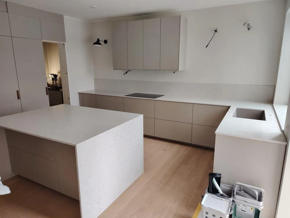 Köksbänkskiva i ljus komposit, Silestone Lime Delight Mocka, med köksö, stänkskydd och induktionshäll i ett kök i Nykvarn.