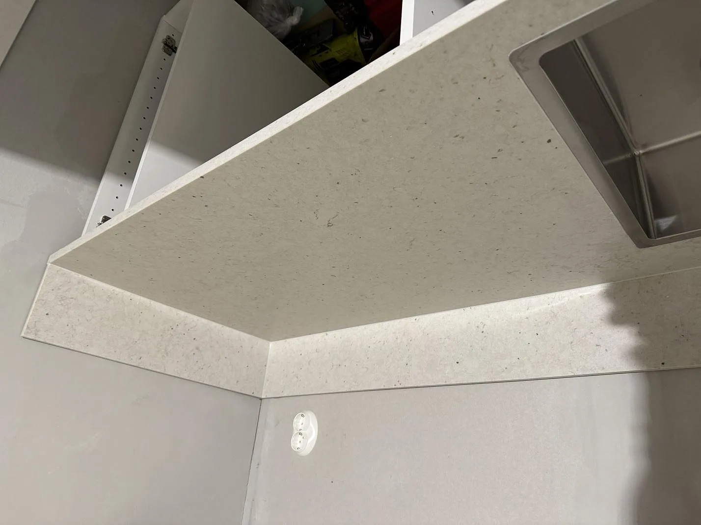 Vinklad detalj av L-formad Silestone Lime Delight bänkskiva, matt beige kvartskomposit, med stänkkant och rostfri ho i kök i Vetlanda.