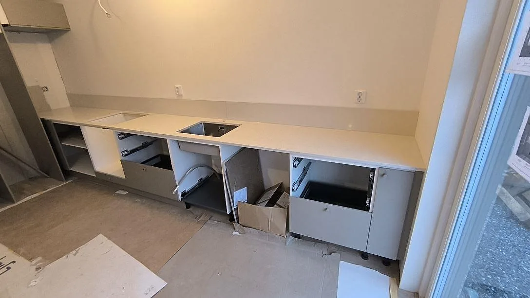 Polerad köksbänkskiva i Silestone Linen Cream med låg stänkkant över öppna köksstommar under montering i Åkersberga.