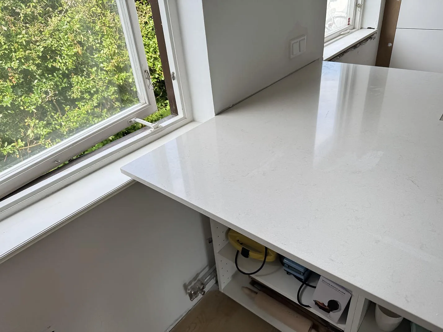 Köksbänkskiva i polerad Silestone Linen Cream, kvartskomposit, vid fönster och öppna stommar i Bunkeflostrand.