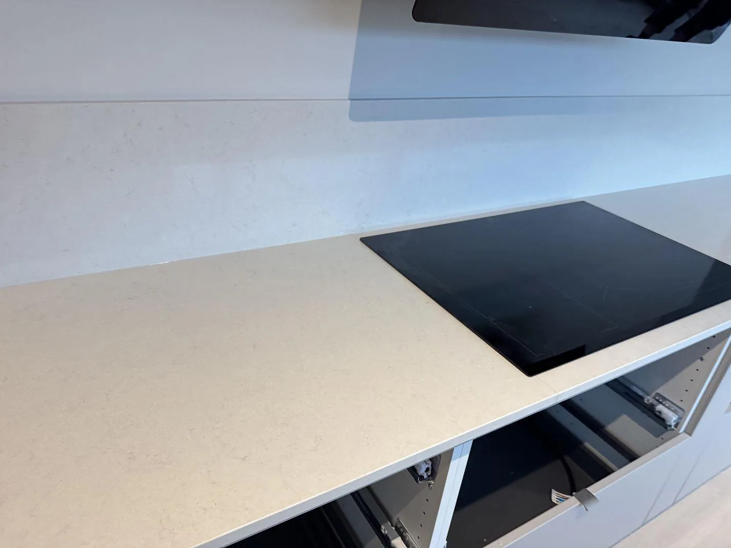 Detalj av svart häll på ljus Silestone Linen Cream kompositbänkskiva med uppvikt stänkskydd i Bunkeflostrand.