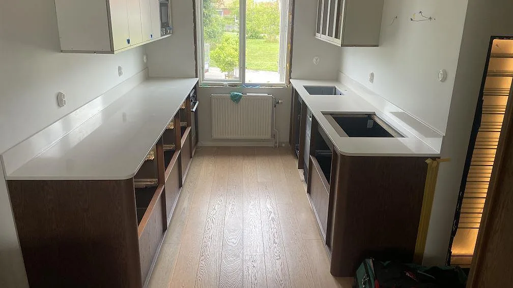 Köksbänkskiva i polerad Silestone Linen Cream komposit med stänkkant, diskhozon och hällöppning i ett kök i Halmstad.