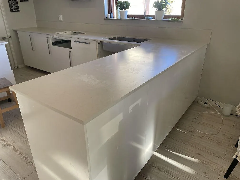 Bred köksbänkskiva i matt Silestone Linen Cream komposit med halvö, rostfri diskho och ljus yta i ett kök i Helsingborg.