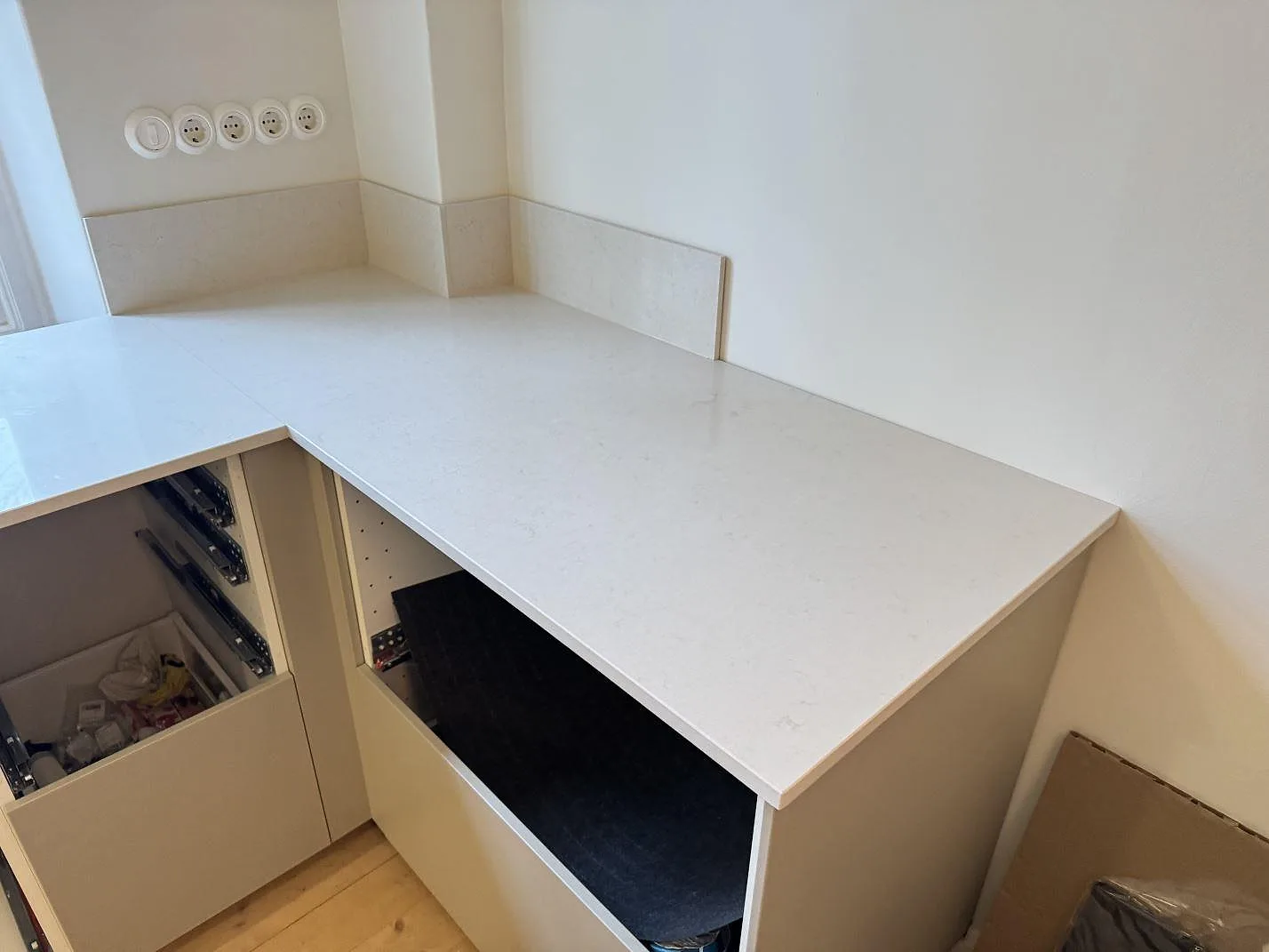 Köksbänkskiva i Silestone Linen Cream, polerad, som vinklar runt ett hörn i L-form med låg stänkkant i ett kök under montering i Helsingborg.