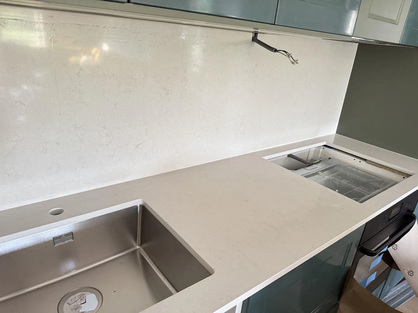 Polerad köksbänkskiva i Silestone Linen Cream med rostfri diskho, ljus kompositskiva och öppet apparaturtag i ett kök i Hjärup.