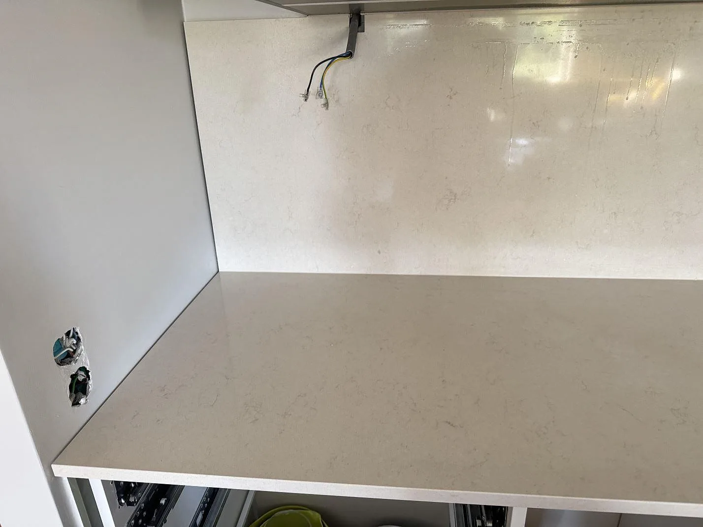 Hörnvy av köksbänkskiva i polerad Silestone Linen Cream med blankt stänkskydd och öppna stommar under montering i Hjärup.