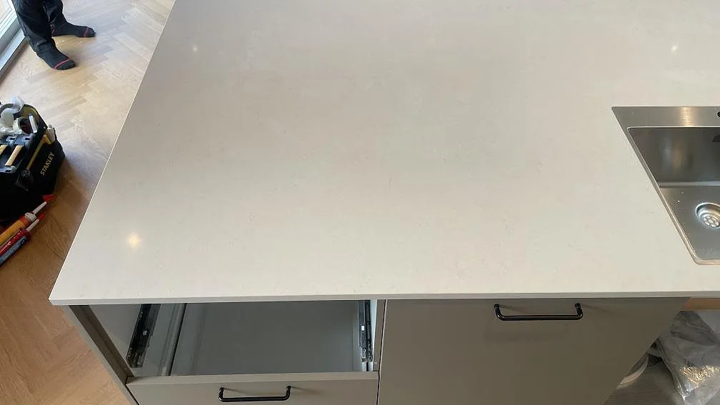 Närbild av köksö i polerad Silestone Linen Cream med ljus ådring, öppna lådor och rostfri diskho synlig vid kanten i Hornslet.