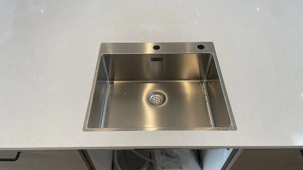 Rostfri diskho i en polerad köksbänkskiva av Silestone Linen Cream, ljus kvartskomposit, monterad i ett kök i Hornslet.