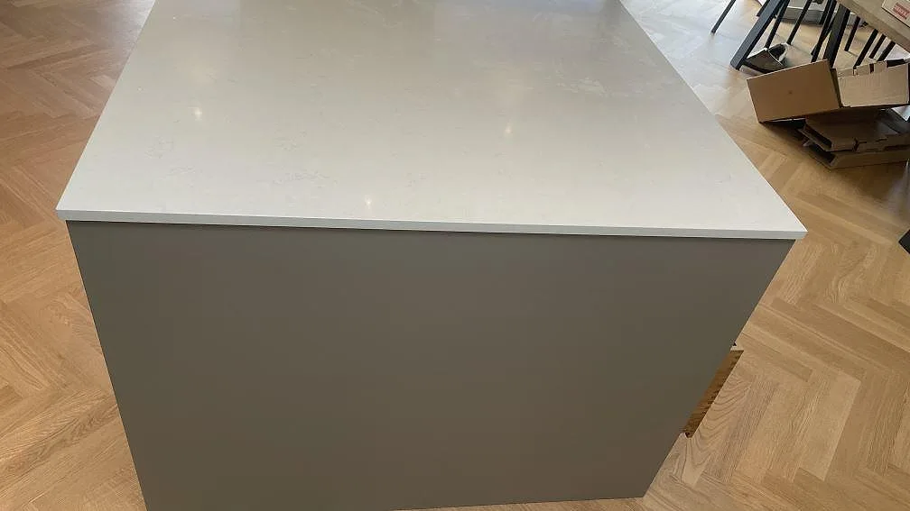 Framkant på köksö i polerad Silestone Linen Cream med ljus komposityta och köksstommar under montering i Hornslet.