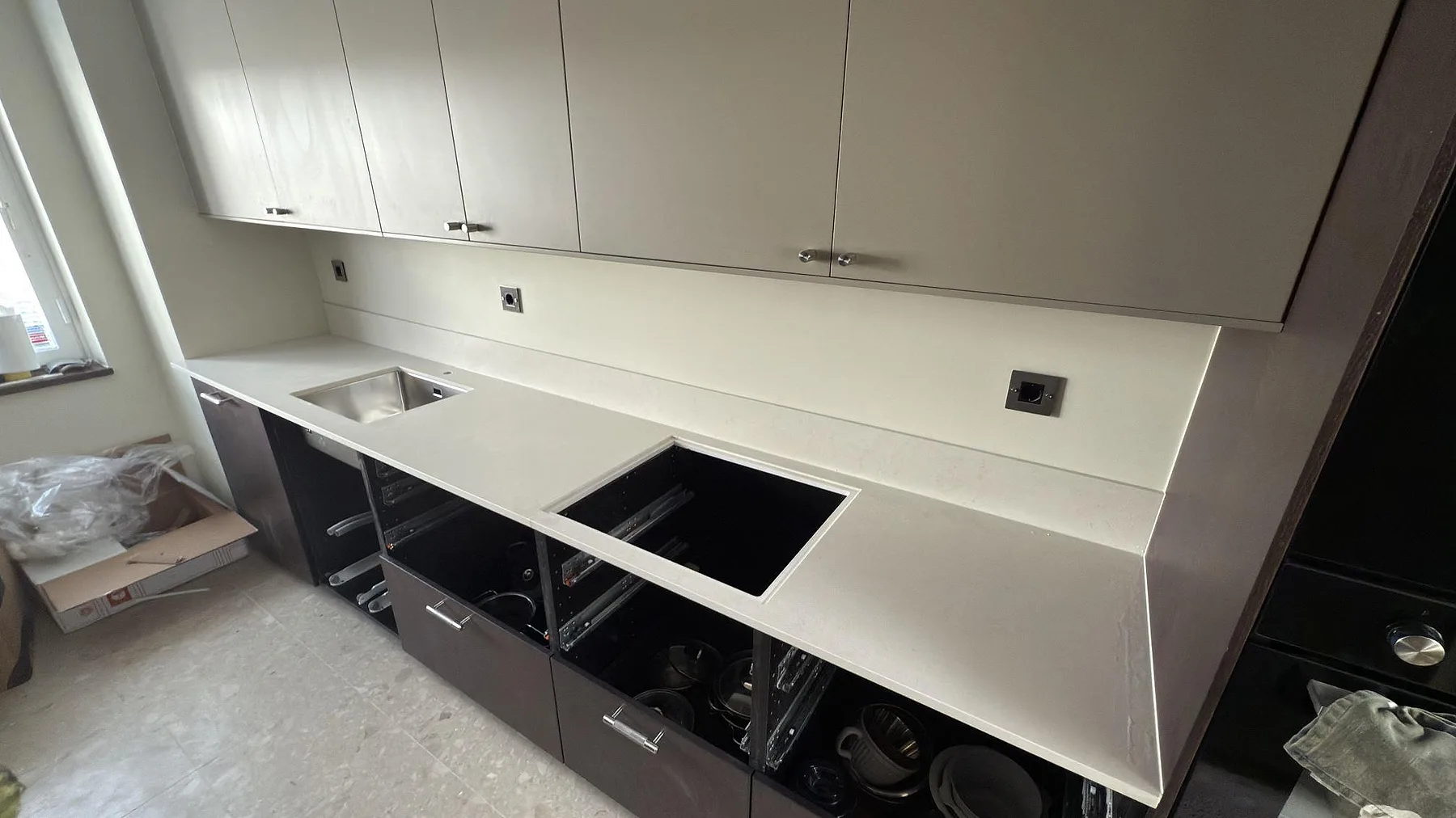 Köksbänkskiva i krämvit matt Silestone Linen Cream med underlimmad rostfri diskho och urtagning för häll i ett kök under montering i Lidingö.