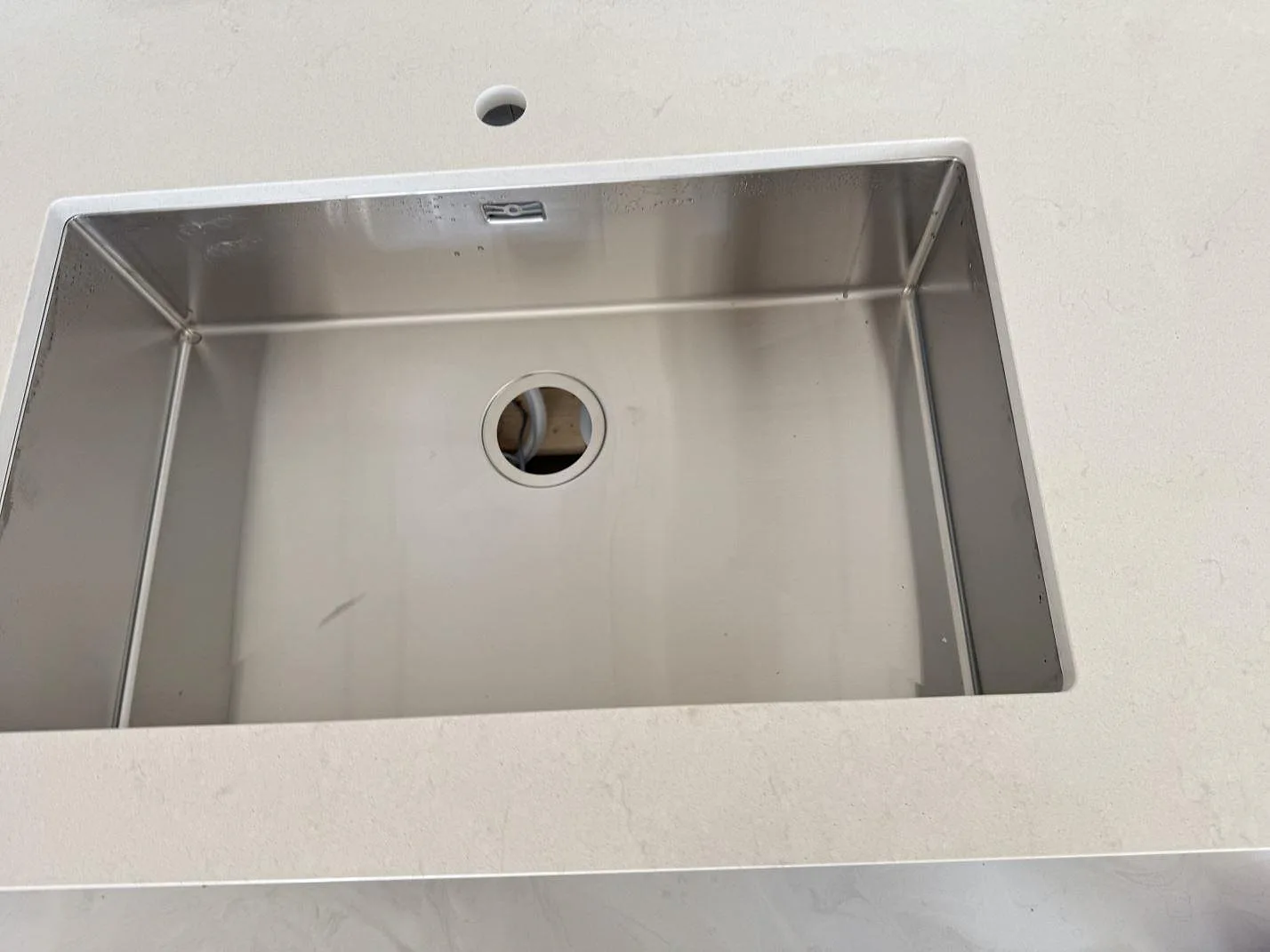 Detalj av rostfri diskho i en köksbänkskiva av polerad Silestone Linen Cream, ljus kvartskomposit, i Lomma.