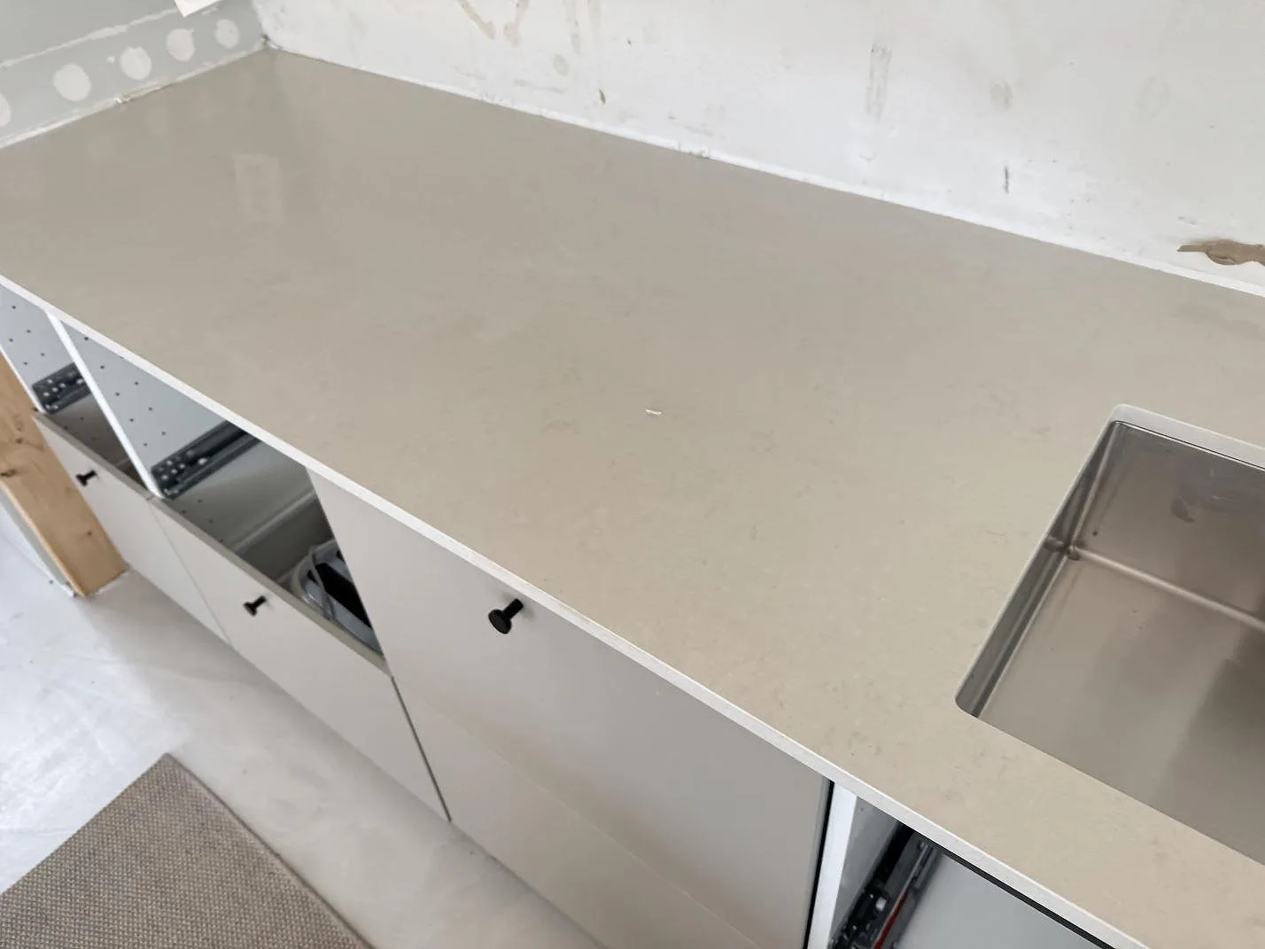 Lång köksbänkskiva i polerad Silestone Linen Cream, ljus kvartskomposit, längs väggen med synlig diskho i Lomma.