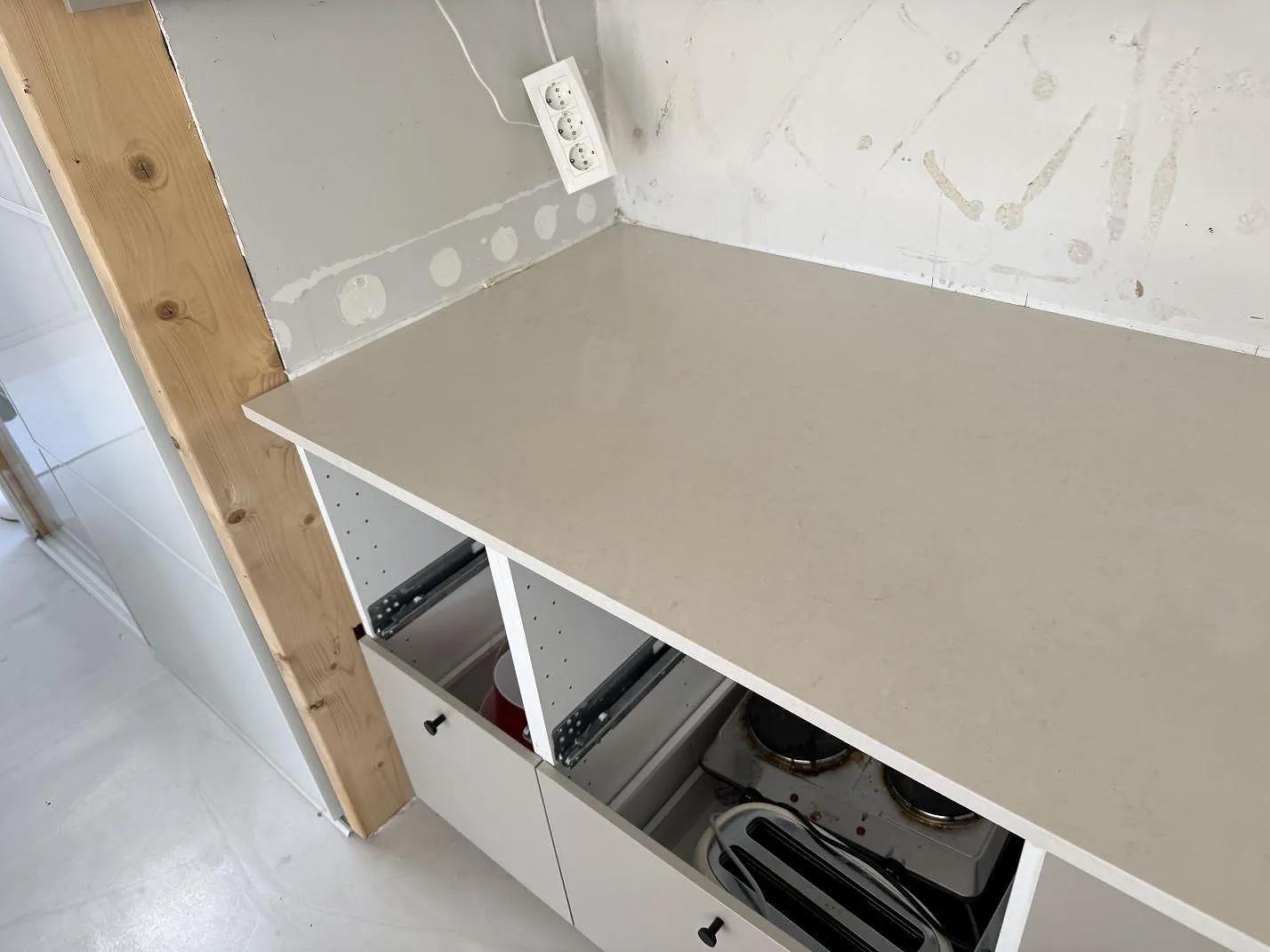 Rak arbetsyta i polerad Silestone Linen Cream, ljus kvartskomposit, över öppna köksstommar och ofärdig vägg i Lomma.