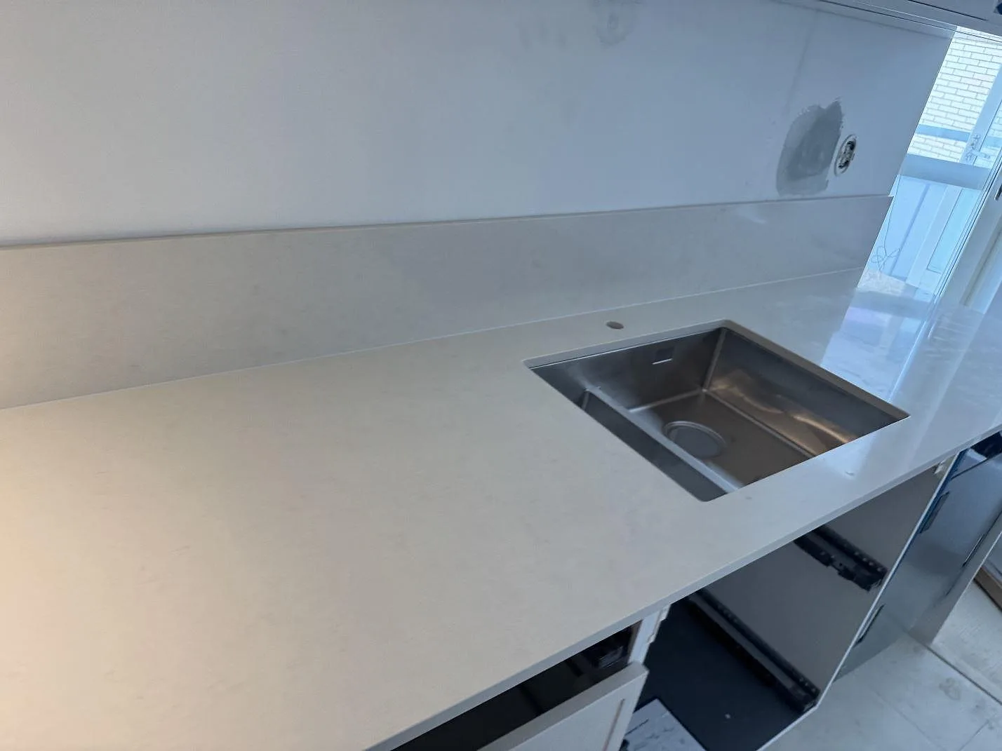 Polerad kompositbänkskiva i Silestone Linen Cream med rostfri diskho och stänkskydd i ett kök i Lund.