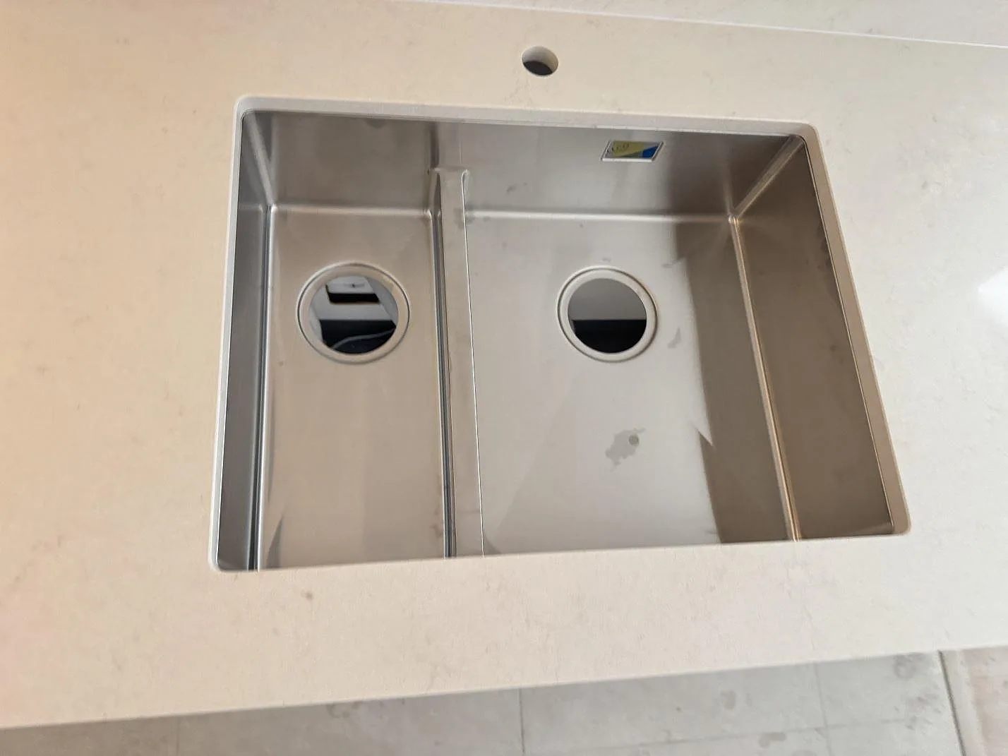 Detalj av rostfri dubbelho i polerad Silestone Linen Cream bänkskiva med blandarhål i Lund.