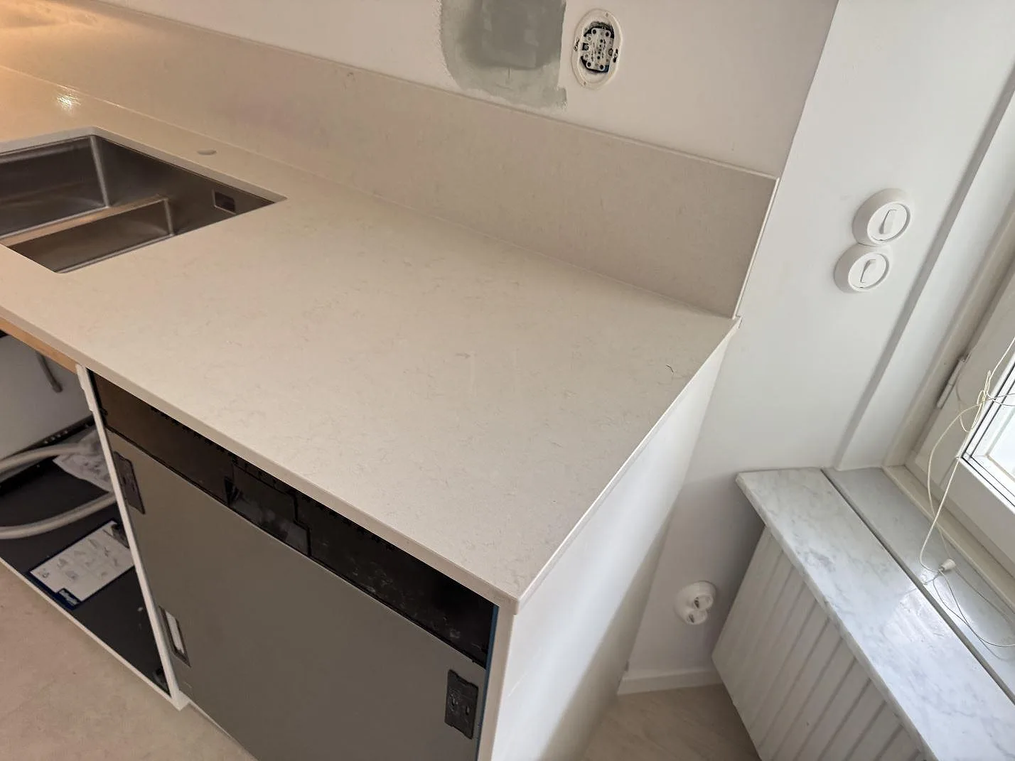 Polerad kompositbänkskiva i Silestone Linen Cream med rostfri diskho, stänkskydd och fönsternära arbetsyta i Lund.