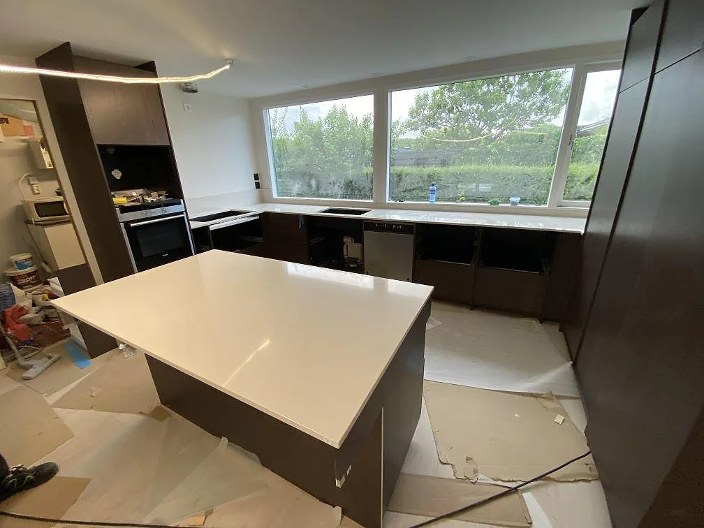 Polerad köksbänkskiva i Silestone Linen Cream komposit med köksö och väggbänk framför stora fönster i Malmö.