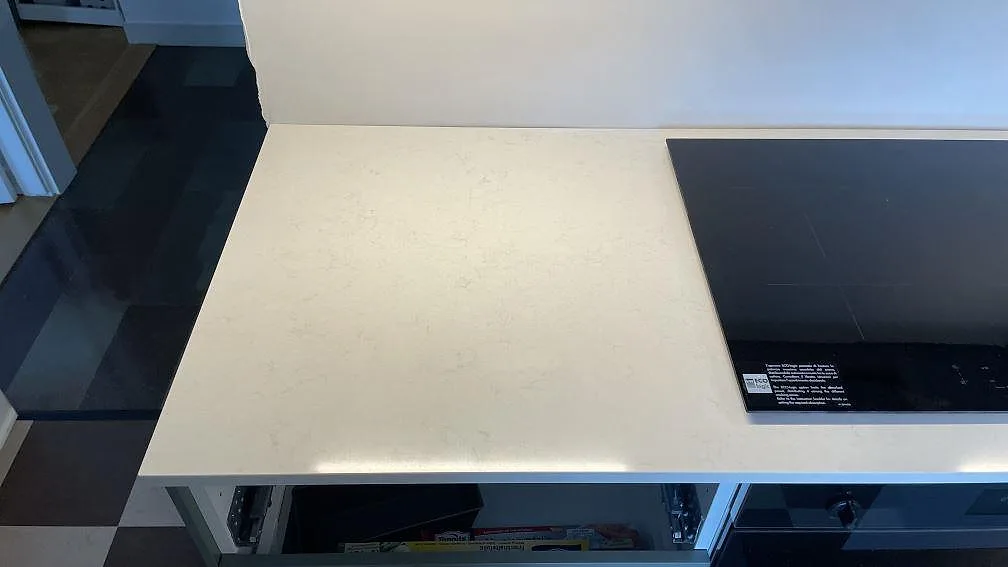 Närbild av polerad Silestone Linen Cream som köksbänkskiva i Malmö, med svart häll och ljus kvartskomposit framför väggen.