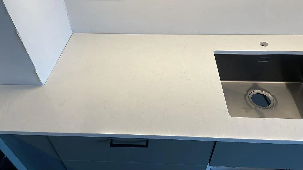 Rak bänksträcka i Malmö med polerad Silestone Linen Cream, ljus kvartskomposit, rostfri diskho och förborrat blandarhål.