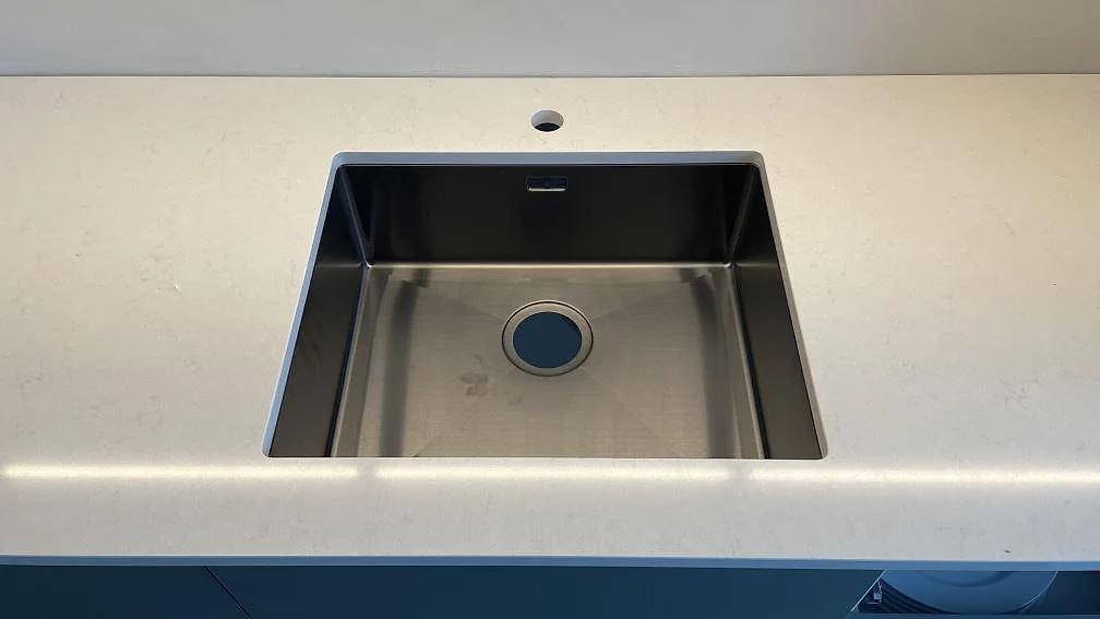 Rostfri diskho i en polerad köksbänkskiva av Silestone Linen Cream, ljus kvartskomposit, i ett kök i Malmö.