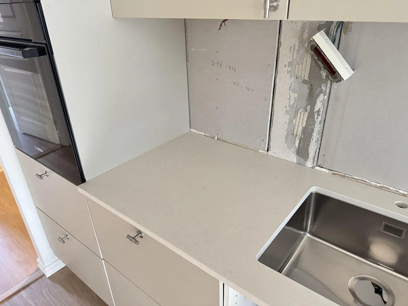 Köksbänkskiva i Silestone Linen Cream, matt krämvit komposit, med underlimmad rostfri diskho och bakomliggande oinredd vägg i ett kök under montering i Malmö.