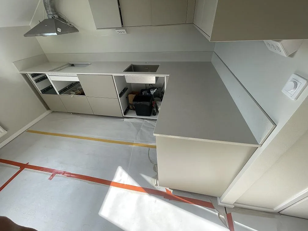 Översikt av L-format kök med bänkskivor i polerad Silestone Linen Cream och öppna stommar under montering i Rönninge.