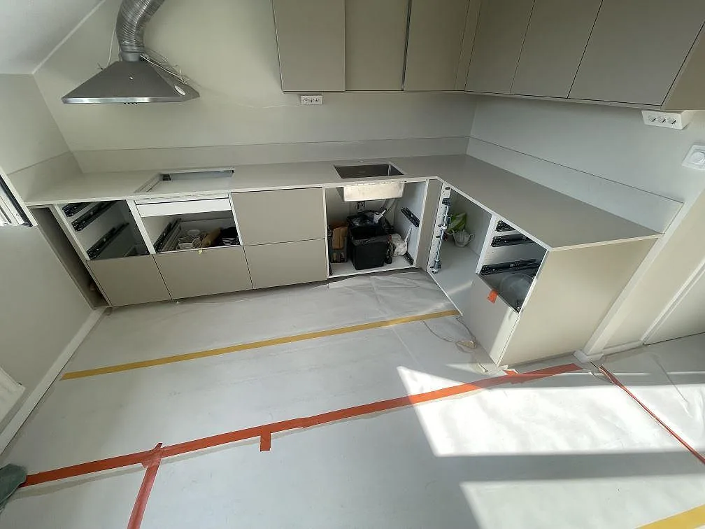 Köksbänkskiva i polerad Silestone Linen Cream, ljus beige komposit, med lågt stänkskydd i ett L-format kök under montering i Rönninge.