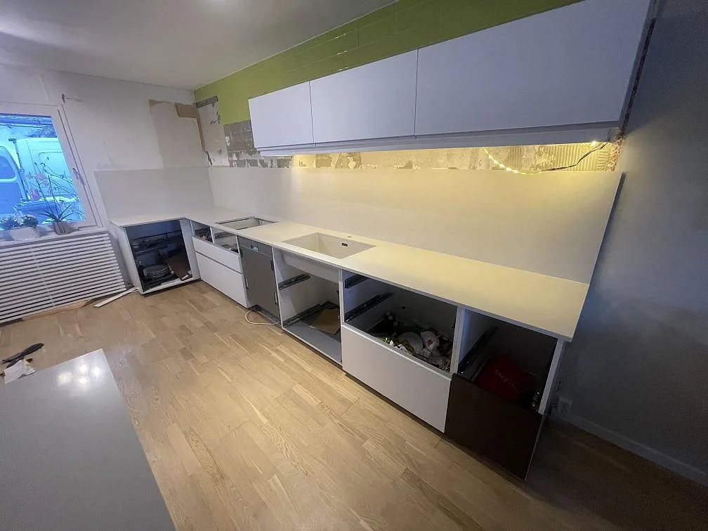 Vägglång köksbänkskiva i krämvit Silestone Linen Cream med urtag för diskho och öppna stommar under installation i Södertälje.