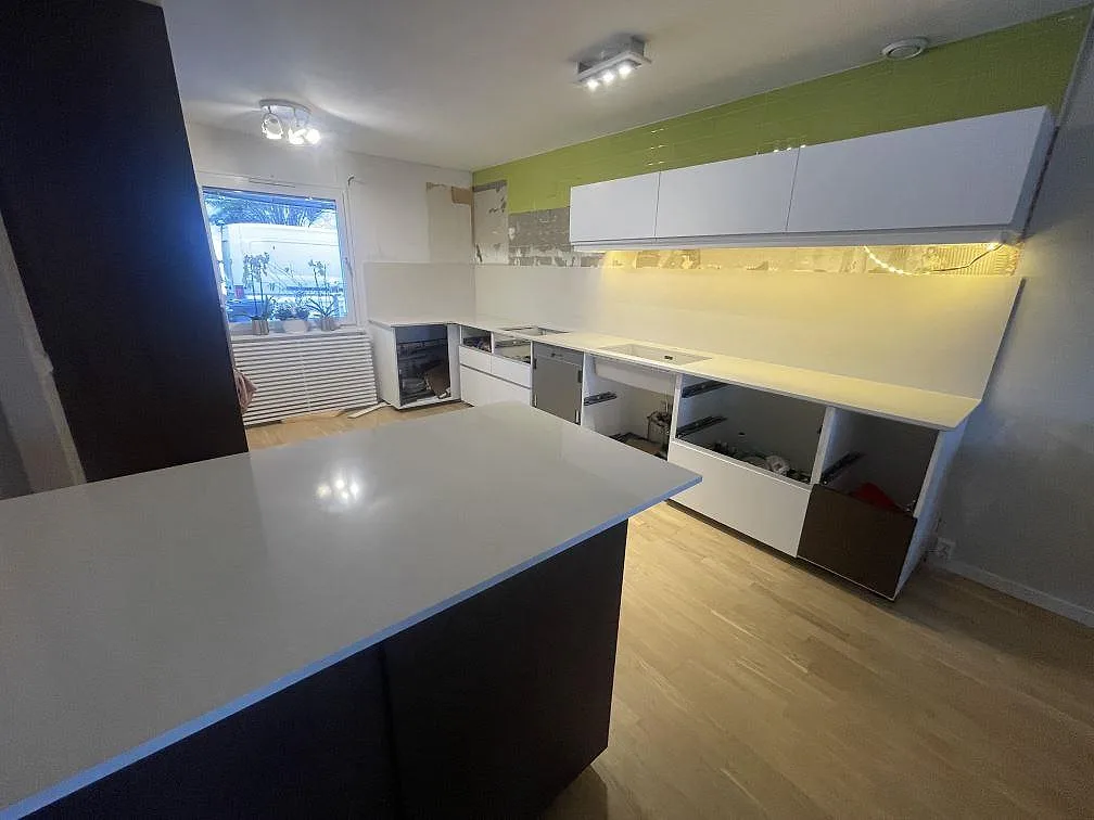 Köksparti i Silestone Linen Cream med halvö och L-format väggrad, polerad komposit, fotograferat under montering i ett kök i Södertälje.