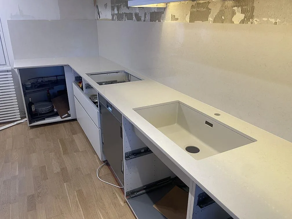 Polerad bänkskiva i Silestone Linen Cream med urtag för häll och en stor underlimmad diskho i komposit i ett kök i Södertälje.