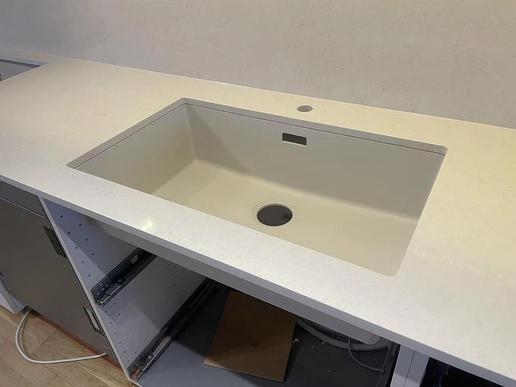 Stor underlimmad diskho i ljus komposit infälld i polerad Silestone Linen Cream med borrat blandarhål i ett kök i Södertälje.