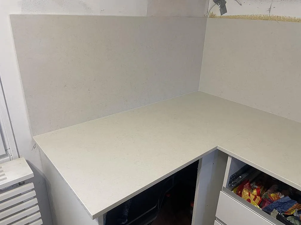 Hörnparti av köksbänkskiva i Silestone Linen Cream med uppvikt stänkkant i samma polerade komposit i ett kök i Södertälje.