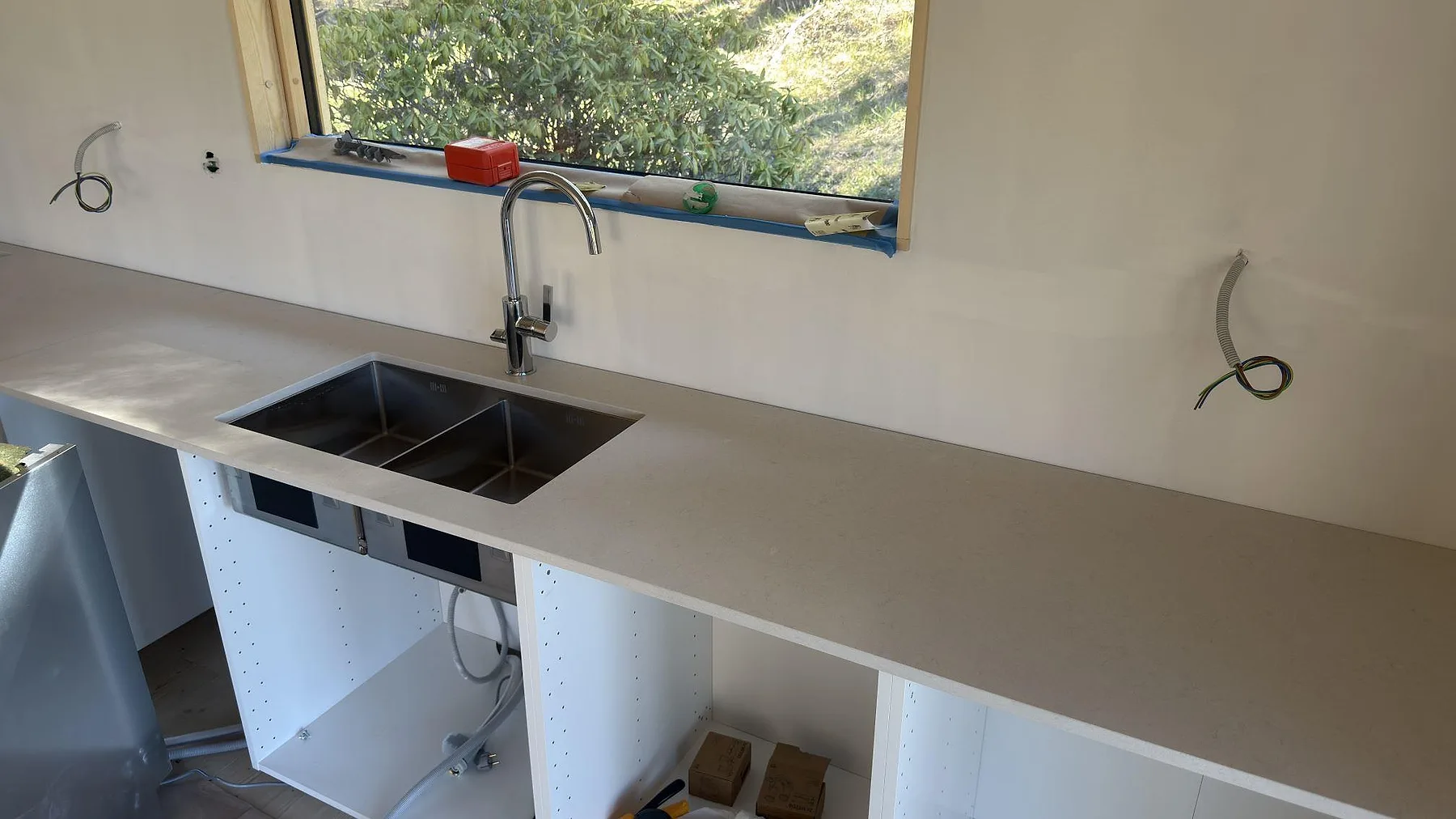 Underlimmad rostfri dubbelho med köksblandare i krom i en matt Silestone Linen Cream-bänkskiva vid köksfönstret i Sorunda.