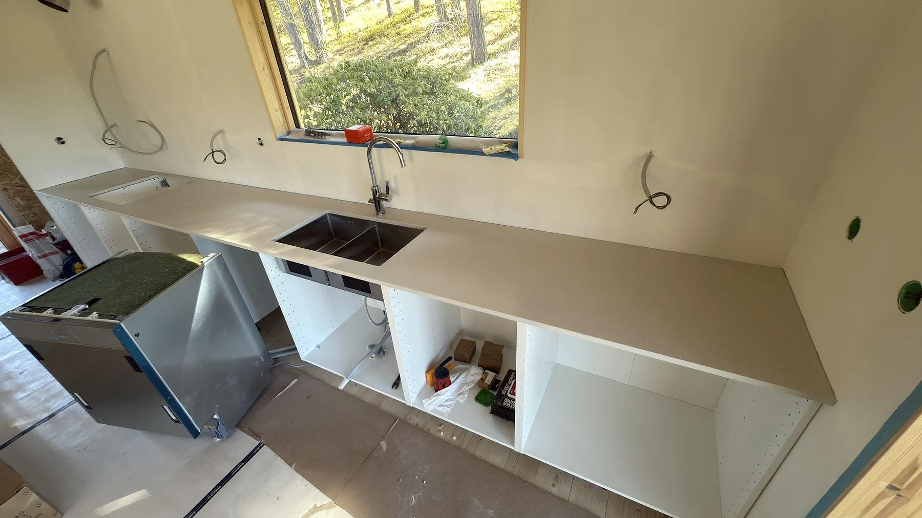 Köksbänkskiva i matt Silestone Linen Cream i ett kök i Sorunda, lång sammanhängande skiva längs fönstervägg med underlimmad rostfri diskho, fotad under montering.