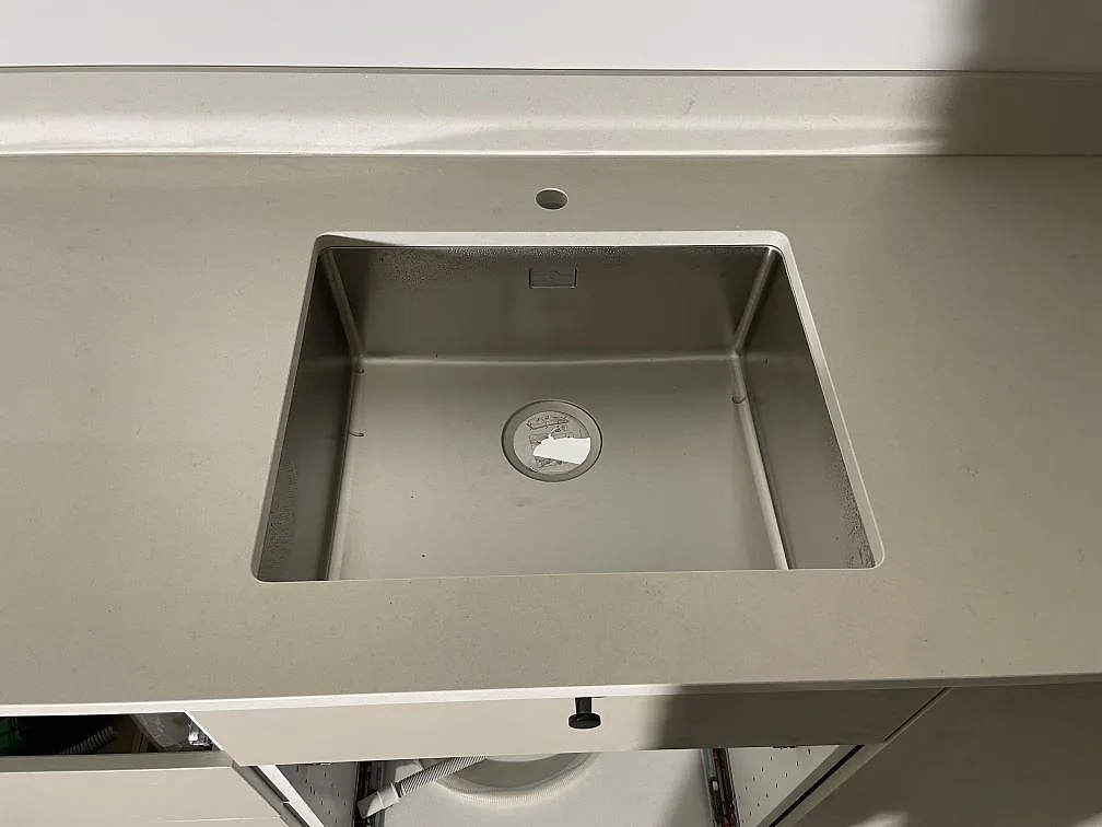 Rostfri diskho monterad under en polerad bänkskiva i Silestone Linen Cream med kranhål och låg stänkkant i ett kök i Stockholm.