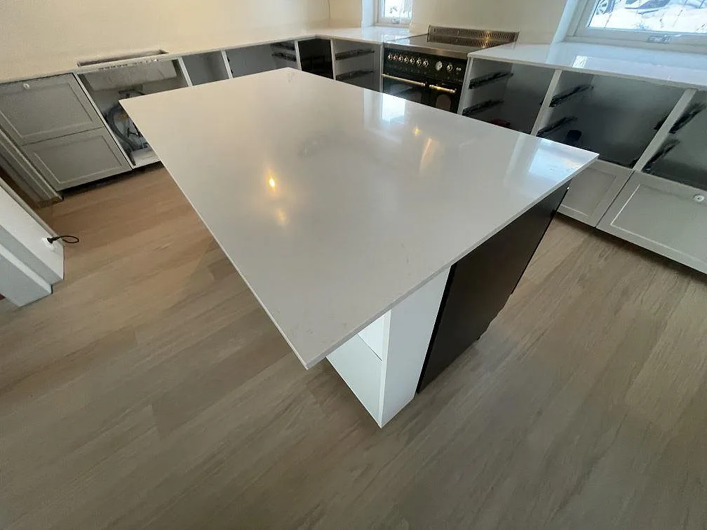 Polerad köksö i Silestone Linen Cream med varm ljusreflex och svart fristående spis i bakgrunden i ett kök i Stockholm.