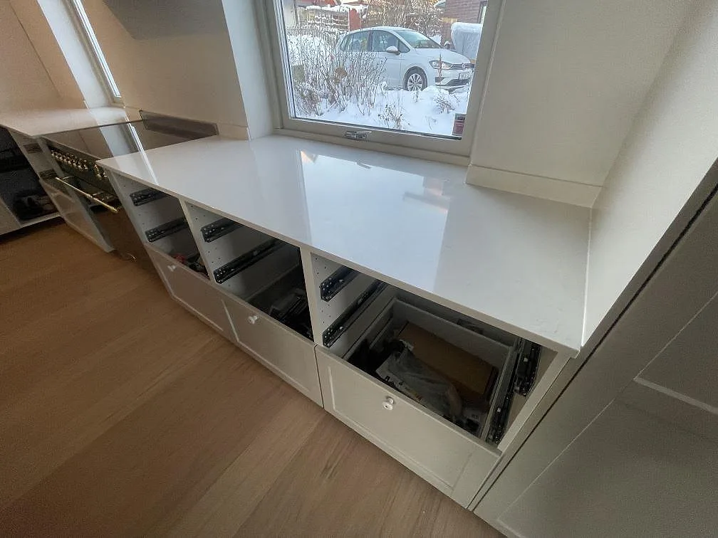 Polerad bänkskiva i Silestone Linen Cream längs fönsterväggen över öppna stommar i ett kök under montering i Stockholm.