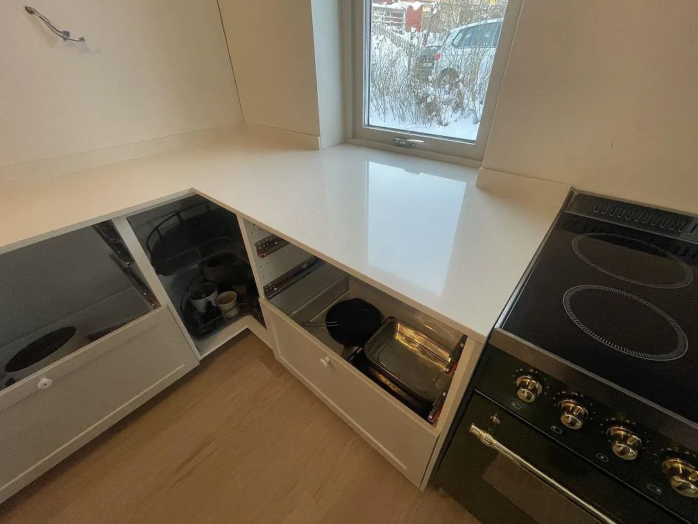 Bänkskiva i Silestone Linen Cream som vänder runt ett hörn mot fönstret, med polerad yta och svart spis i ett kök i Stockholm.