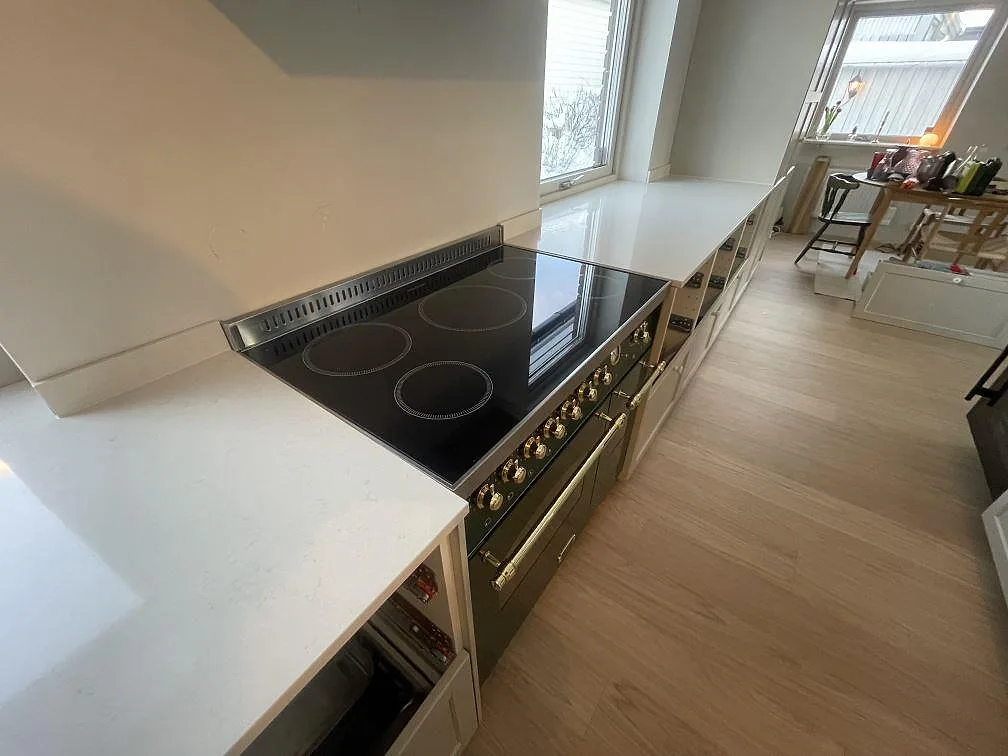 Fristående induktionsspis i svart glas inramad av bänkskivor i polerad Silestone Linen Cream i ett kök i Stockholm.