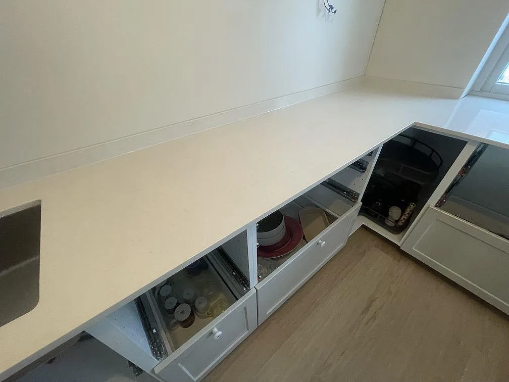 Lång bänkskivelängd i polerad Silestone Linen Cream med fönsterbänk och öppna lådor i ett kök under montering i Stockholm.